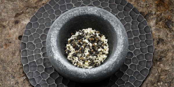 A grey stone serving bowl on a grey plate with frozen tunworth, malt crumb, preserved damsons and lemon thyme