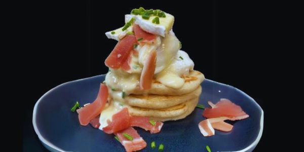 Pikelet pancakes with Tunworth, Hollandaise and Speck, garnished with chives, served on a blue ceramic plate